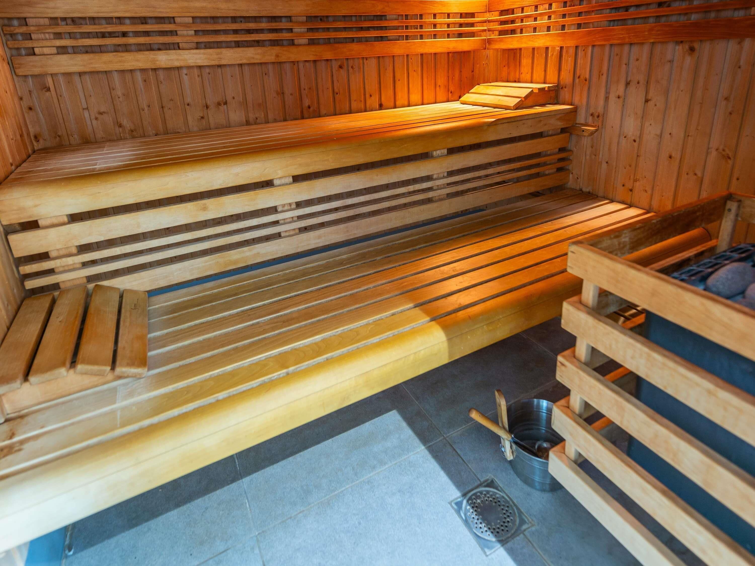Un sauna avec des bancs en bois et un seau en métal.