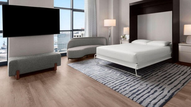 A modern hotel room with a large bed, a sofa, a TV, and a city view.