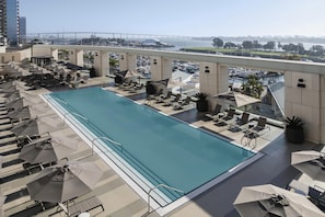 Une piscine sur le toit, dotée de chaises longues et de parasols, avec vue sur un pont et une marina en arrière-plan.