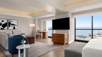 Una habitación de hotel moderna con una cama grande, un televisor de pantalla plana, un escritorio, un sofá y vista al mar.