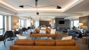Un hall d’hôtel spacieux avec un espace salon central, plusieurs fauteuils, un canapé, une table basse et un téléviseur.