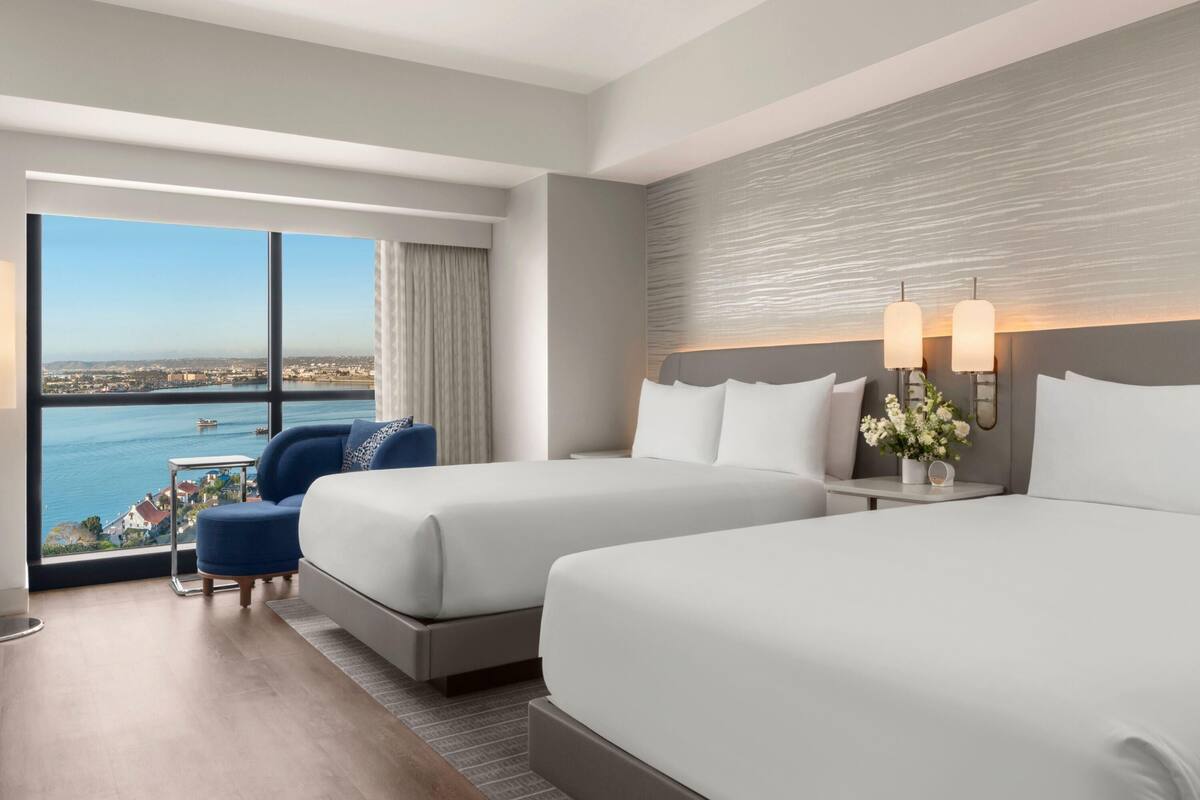 A hotel room with two beds, a sofa, a view of the sea, and a cityscape.