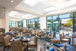 A spacious hotel dining area with multiple tables and chairs, large windows, and a view of the outdoors. - Manchester Grand Hyatt San Diego (San Diego)