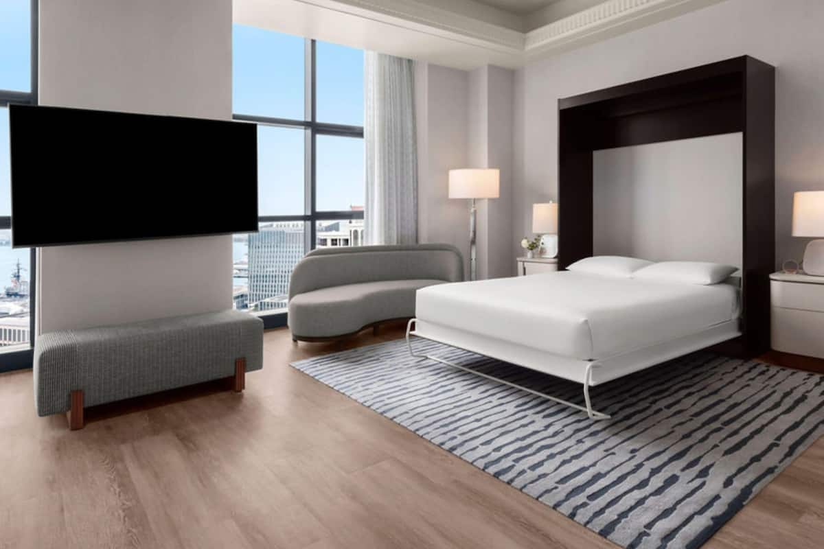 Une chambre d’hôtel moderne avec un grand lit, un canapé, une télévision et une vue sur la ville.