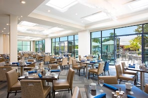 A spacious hotel dining area with multiple tables and chairs, large windows, and a view of the outdoors. - Manchester Grand Hyatt San Diego (San Diego)