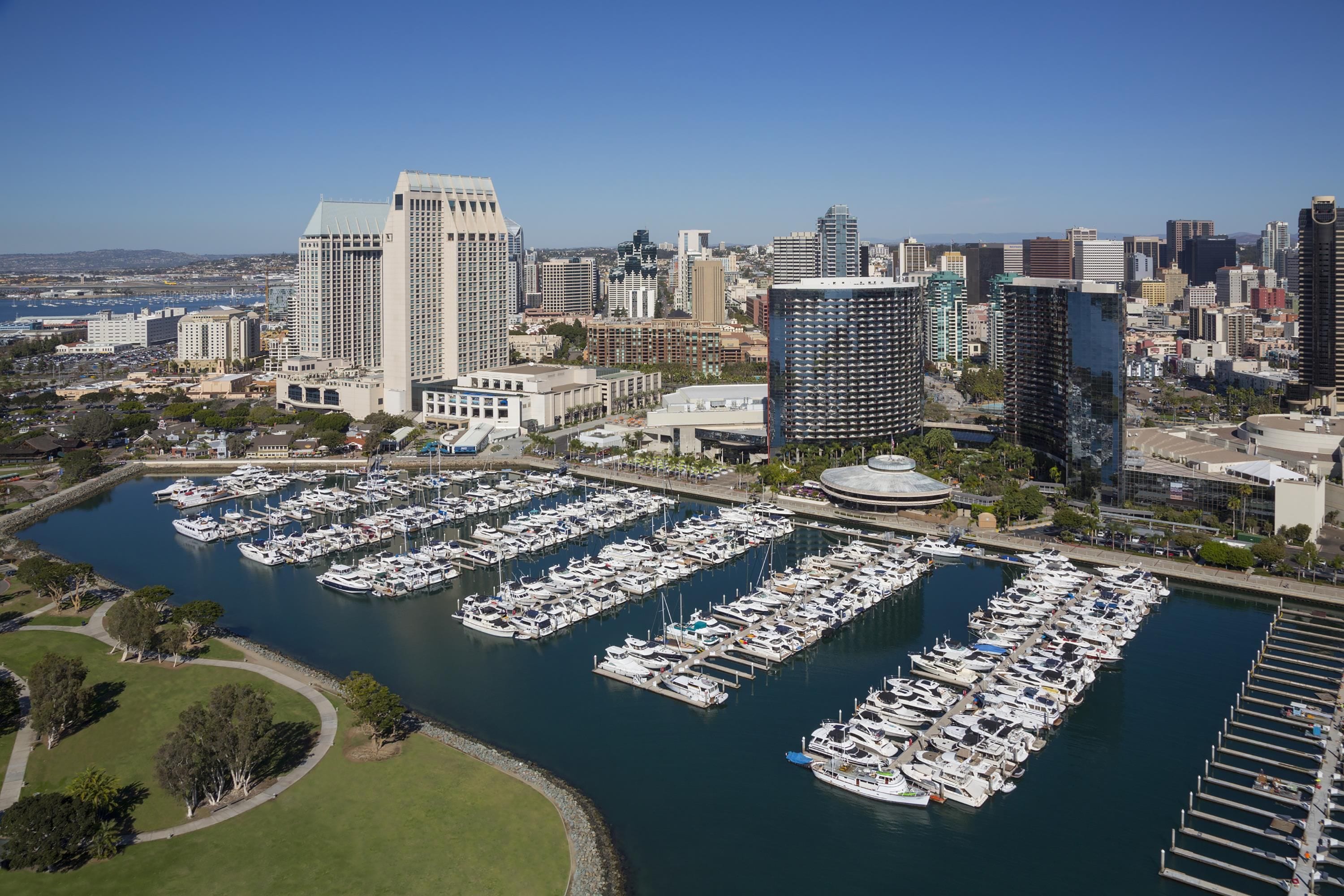 A marina with numerous boats docked, surrounded by city buildings and a clear sky.