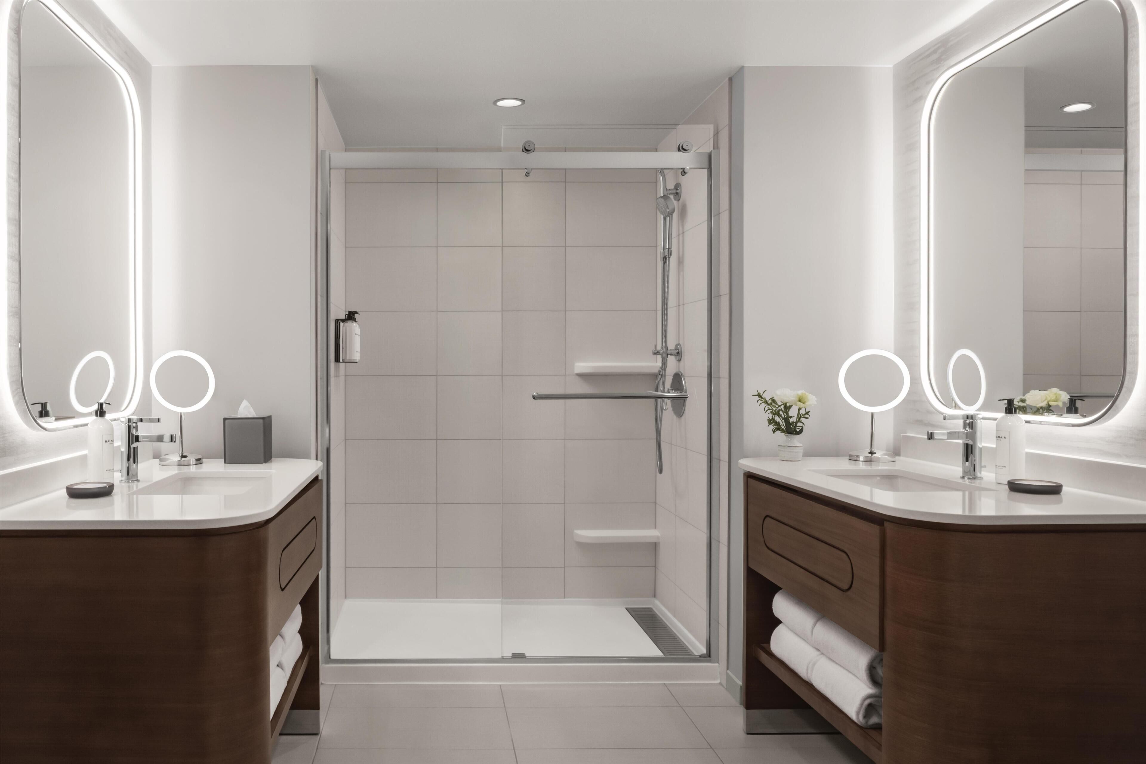A modern bathroom with two sinks, a shower, and a glass door.