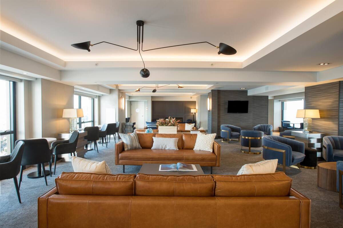 A spacious hotel lobby with a central seating area, multiple armchairs, a sofa, a coffee table, and a television.