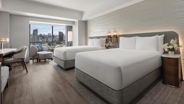 Une chambre d’hôtel avec deux lits, un bureau, une chaise et une vue sur la ville.
