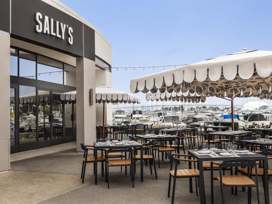 An outdoor dining area with tables and chairs, a covered seating area, and a view of boats in the background.