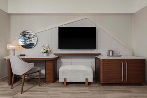 A modern room with a flat-screen TV mounted on a wall, a wooden desk with a chair, a small white ottoman, and a cabinet with drawers. - Manchester Grand Hyatt San Diego (San Diego)