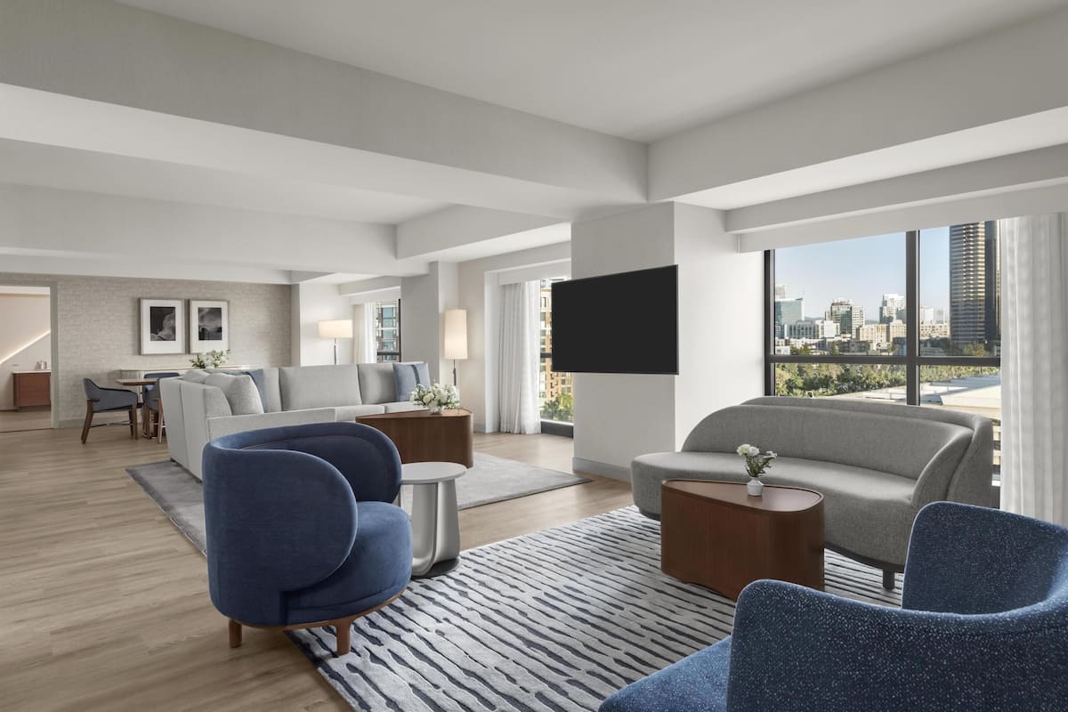 A modern living room with a sofa, chairs, a TV, and a city view.