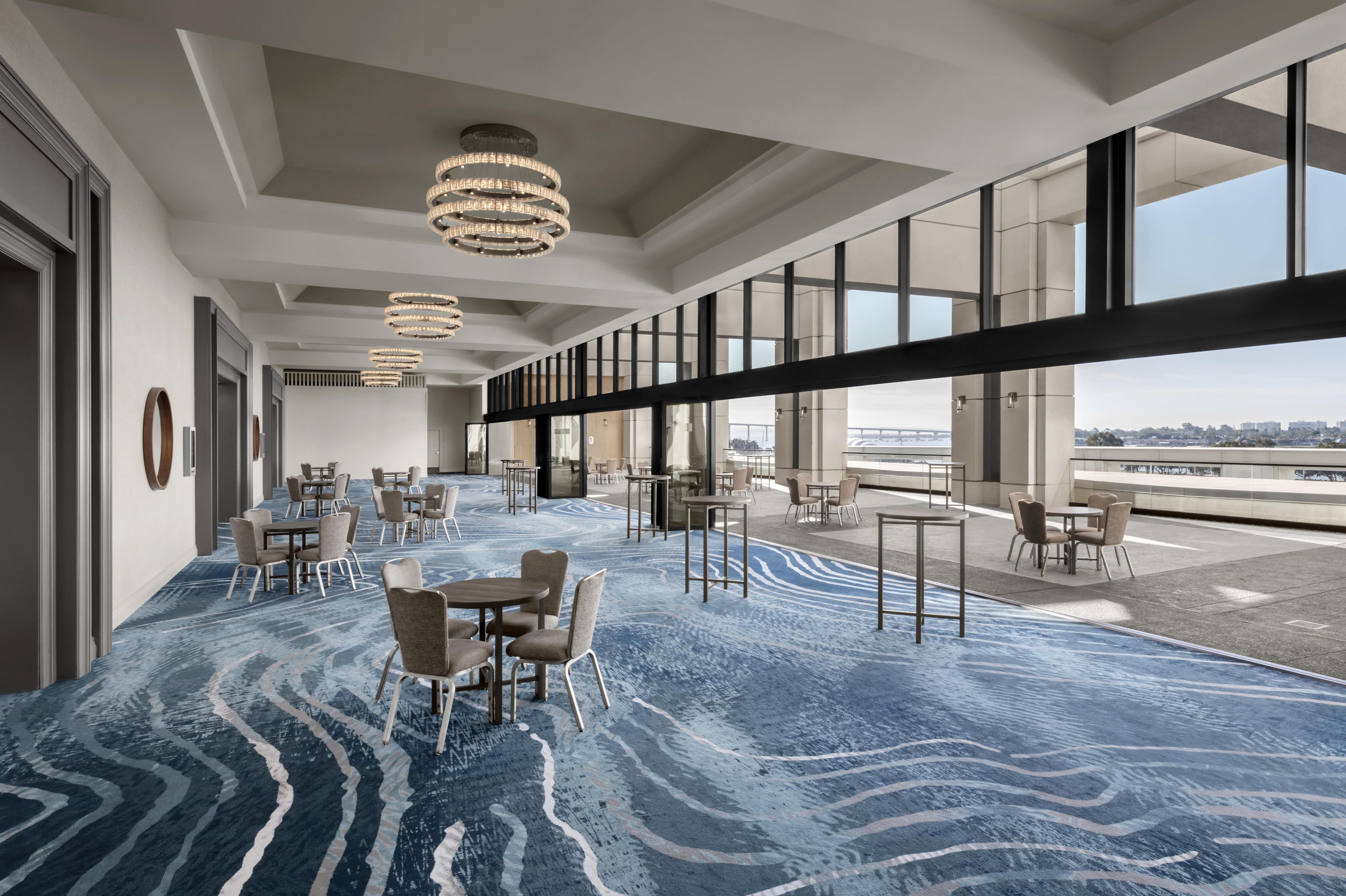 Eine moderne Hotellobby mit blauem Teppichmuster, mehreren Sitzbereichen und großen Fenstern, die einen Blick auf die Stadt bieten.