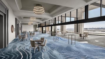 Un moderno vestíbulo de hotel con alfombra de diseño azul, varias zonas de estar y amplias ventanas con vistas a la ciudad.