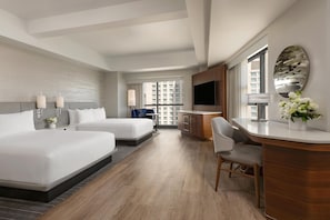 Une chambre d’hôtel avec deux lits, un bureau, une télévision et une grande fenêtre donnant sur la ville.