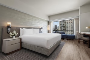A modern hotel room with a large bed, bedside tables, a desk, and a view of a cityscape through large windows. - Manchester Grand Hyatt San Diego (San Diego)