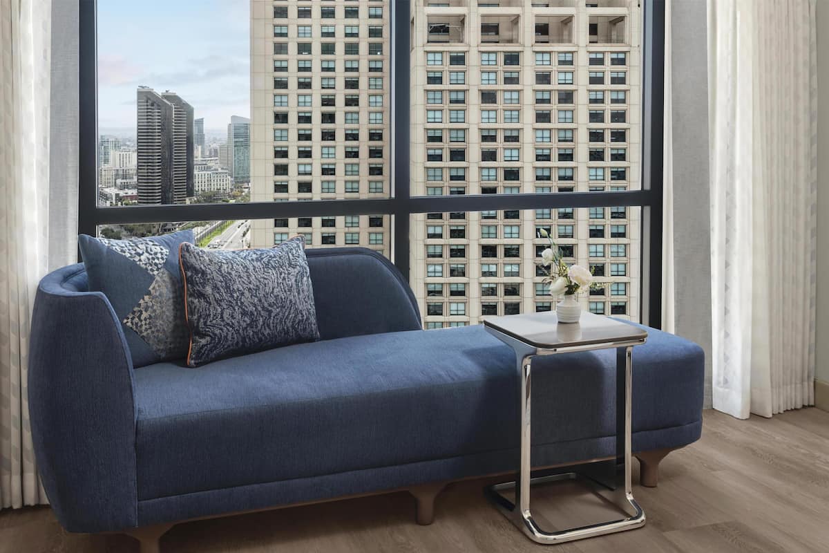 Un salon moderne avec un canapé bleu, une petite table d’appoint et une vue sur des immeubles de grande hauteur à travers de grandes fenêtres.