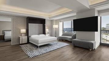 A modern hotel room with a large bed, a flat-screen TV, a sofa, and a view of the city.