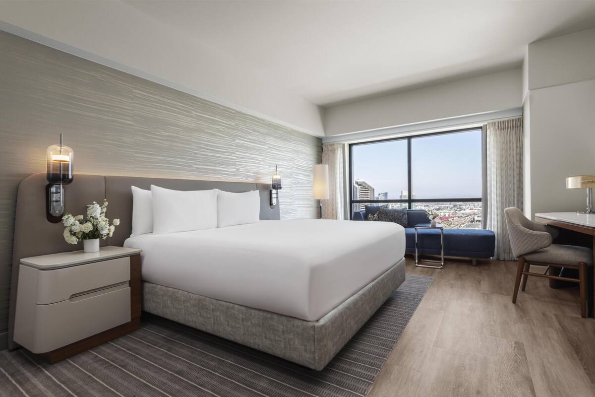 A modern hotel room with a large bed, a desk, and a view of the city.