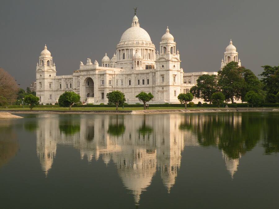 Un edificio grande, blanco e histórico con múltiples cúpulas y ventanas de arco, reflejado en aguas tranquilas.