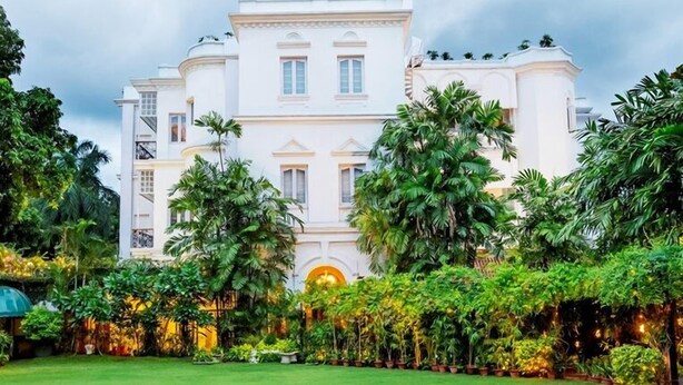 Un edificio grande y blanco con fachada simétrica, rodeado de exuberante vegetación y un césped bien cuidado.