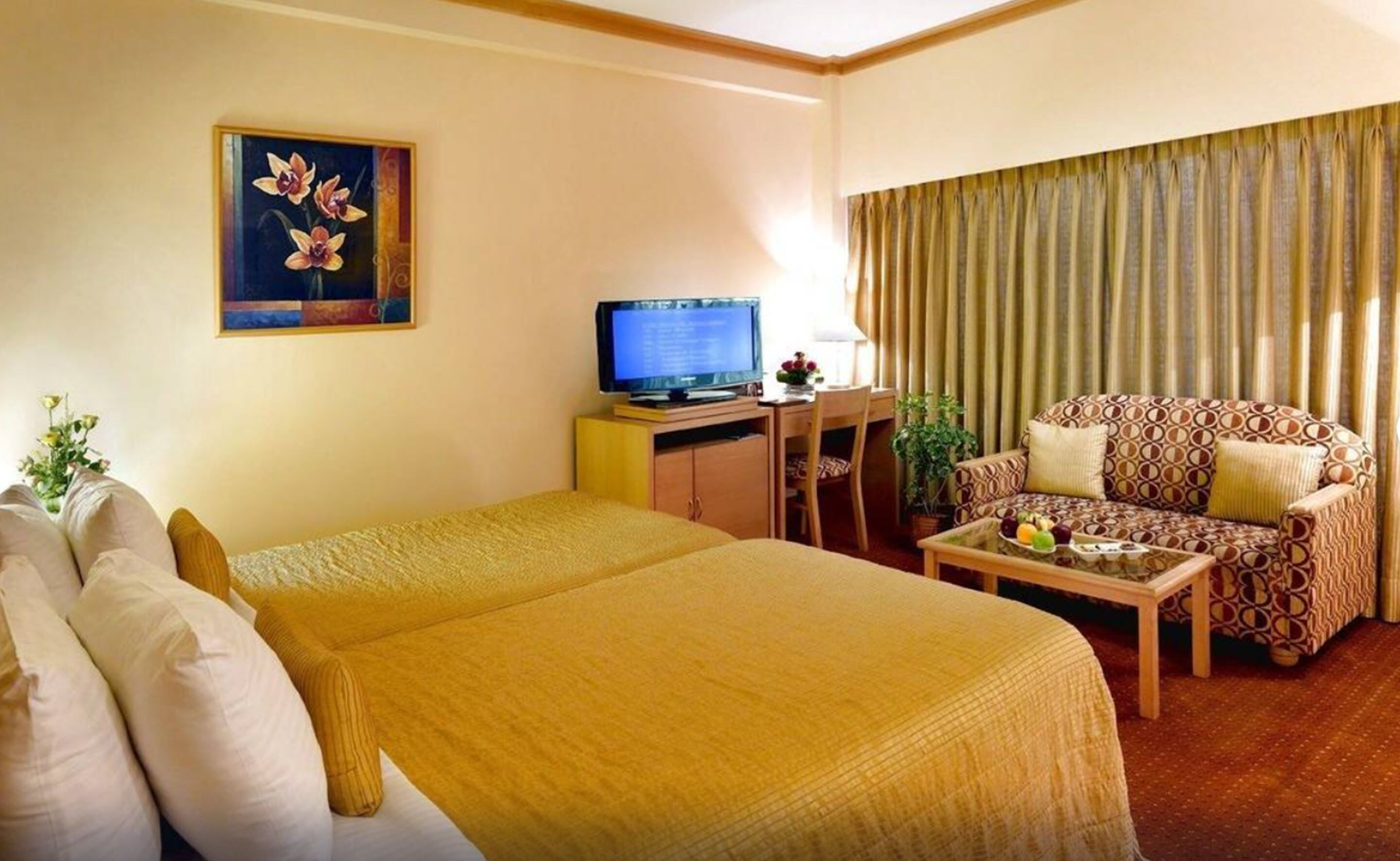 A hotel room with a bed, a sofa, a television, and a painting on the wall.