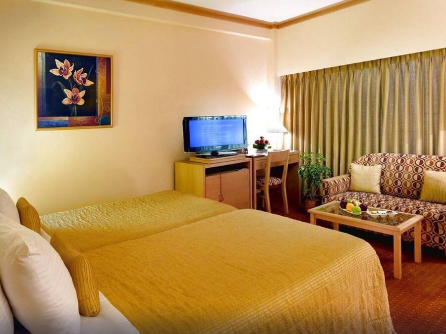 A hotel room with a bed, a sofa, a television, and a painting on the wall.