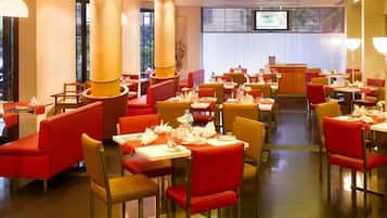 Ein Restaurant mit roten Sitzbänken und Tischen, großen Säulen und einem Fernseher an der Wand.