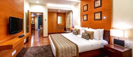 Une chambre d’hôtel avec un plancher en bois, un lit recouvert d’une couvre-lit à motifs, un téléviseur posé sur un meuble en bois, une table de chevet avec une lampe, et un mur orné de tableaux encadrés.