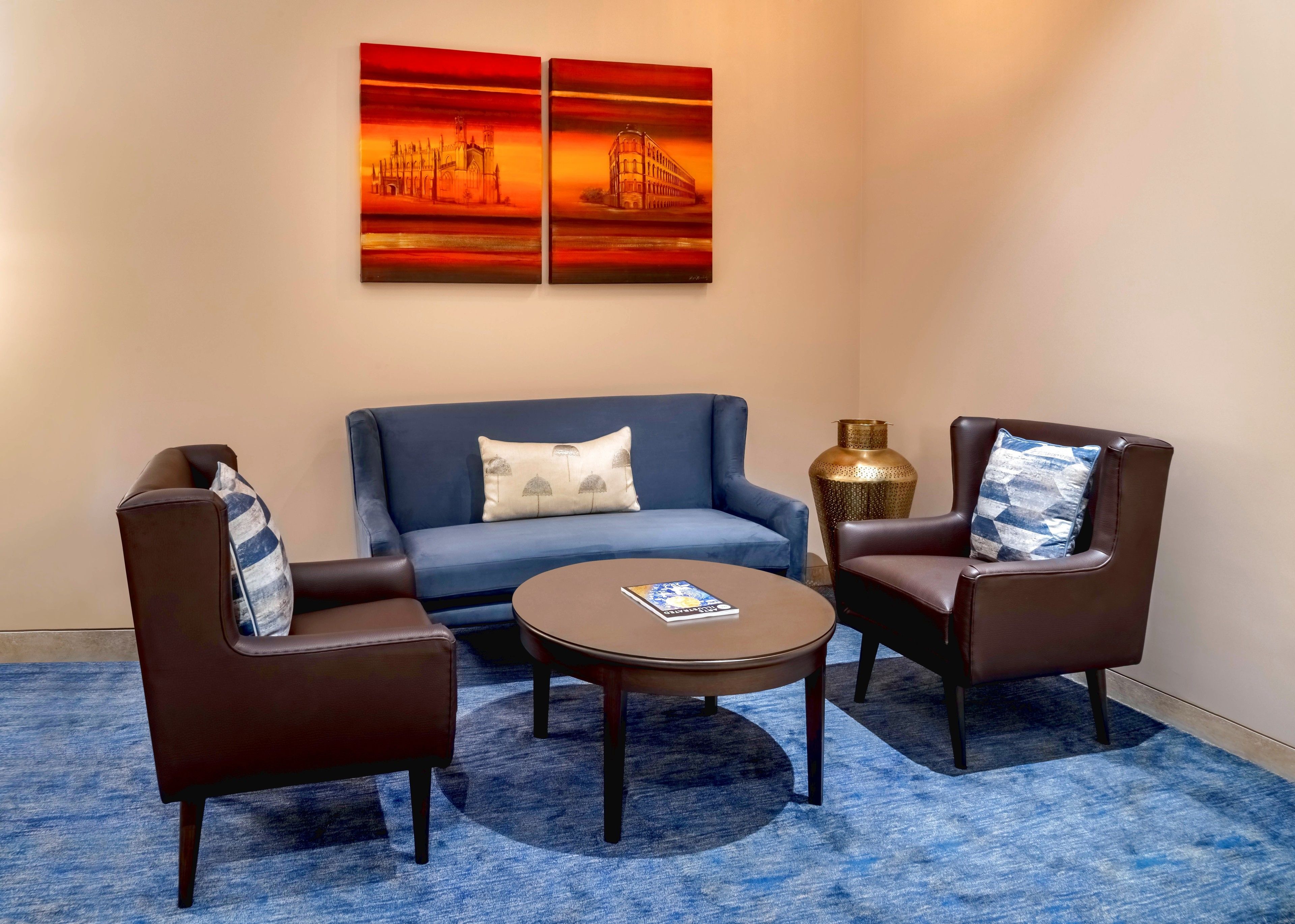 A room with a blue sofa, two brown armchairs, a round coffee table, and a large vase.