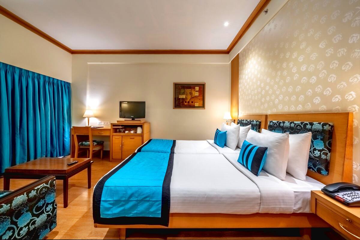 A hotel room with a bed, a desk with a computer, a television, and a patterned headboard.
