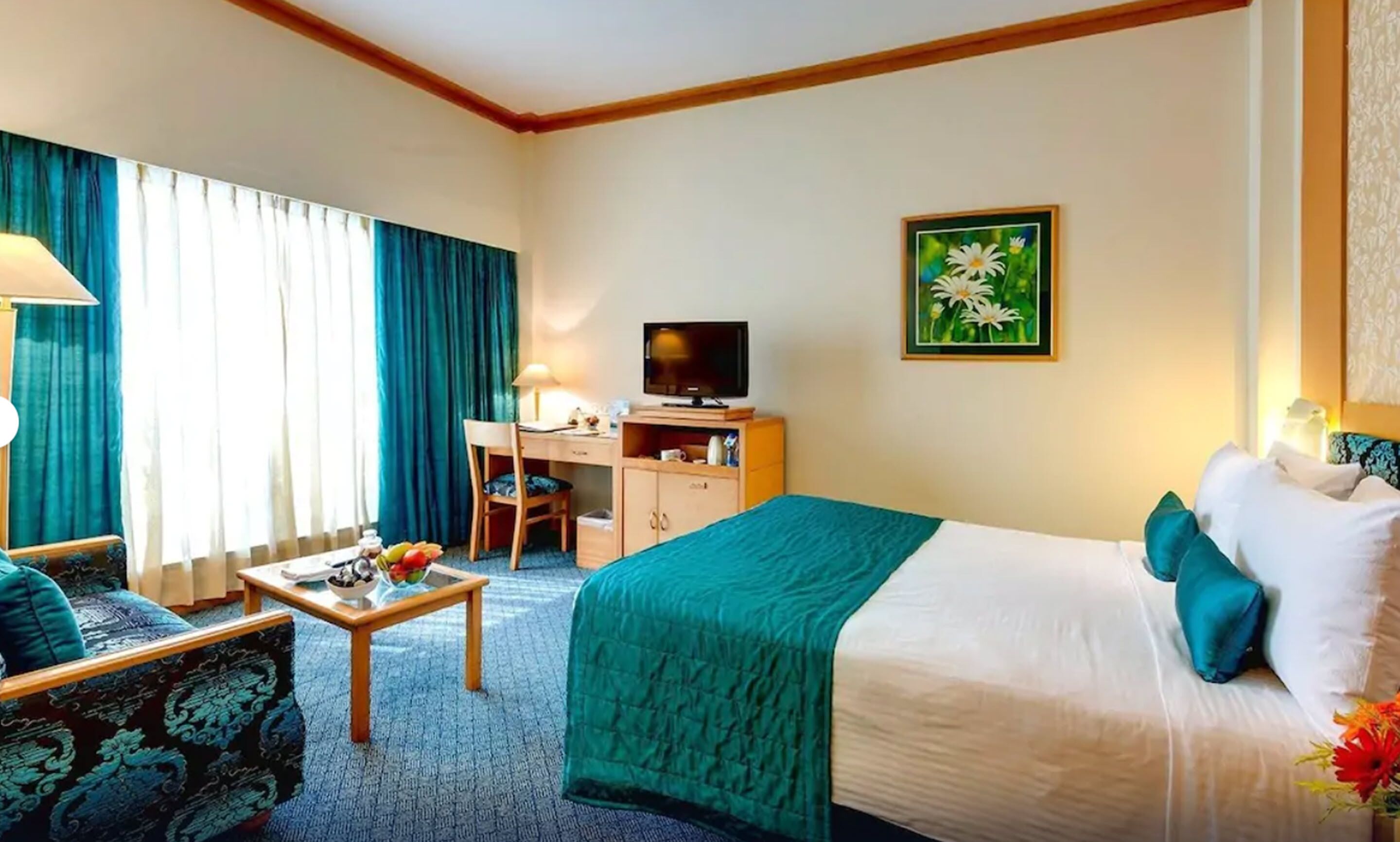 A hotel room with a bed, a desk, a chair, a television, and a painting on the wall.