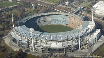 Vista aérea de un estadio con césped central, asientos alrededor y varias torres de iluminación.