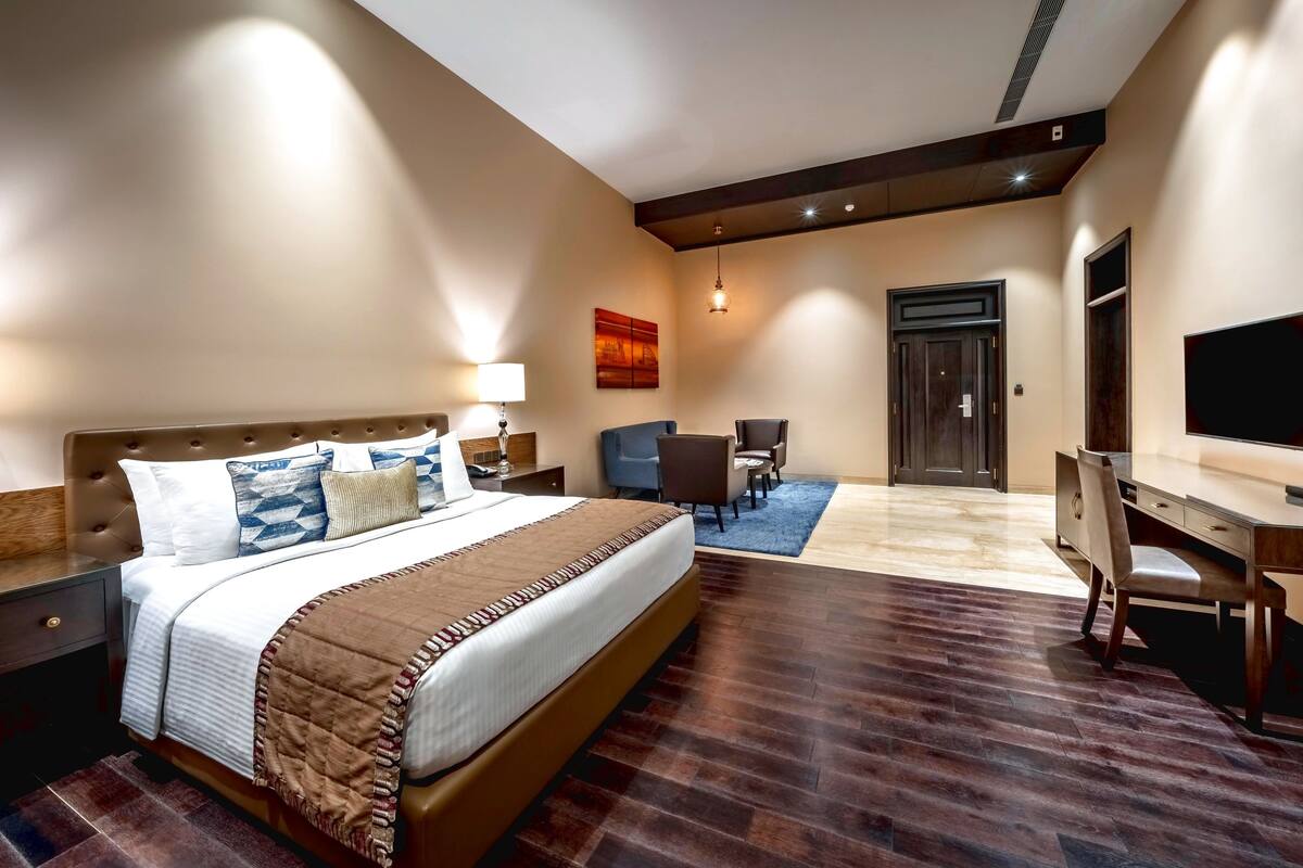 A hotel room with a large bed, a desk, a chair, a TV, and a door.