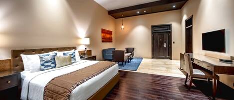 Habitación de hotel con una cama grande, un escritorio, una silla, un televisor y una puerta.
