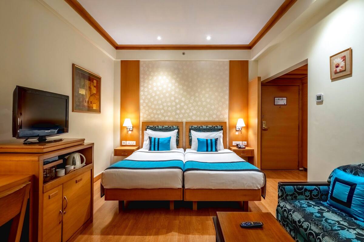A hotel room with two beds, a TV, a desk, and a sofa.