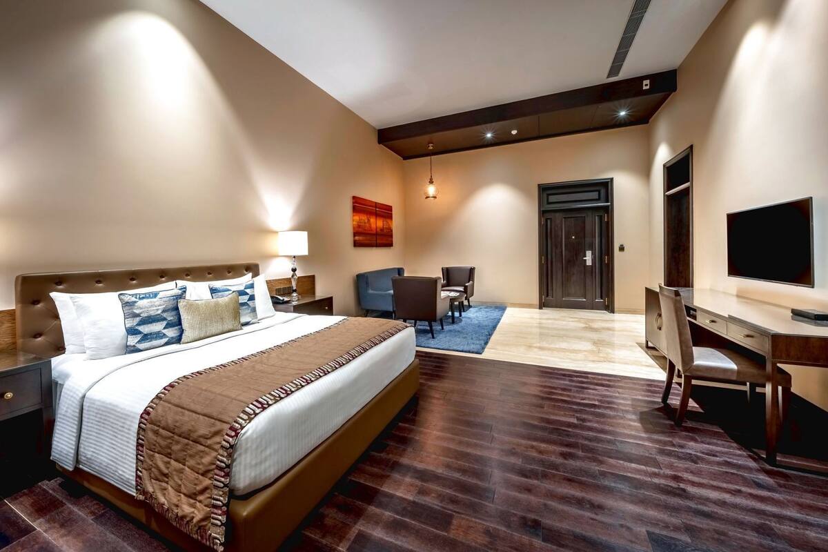 A hotel room with a large bed, a desk, a chair, a TV, and a door.