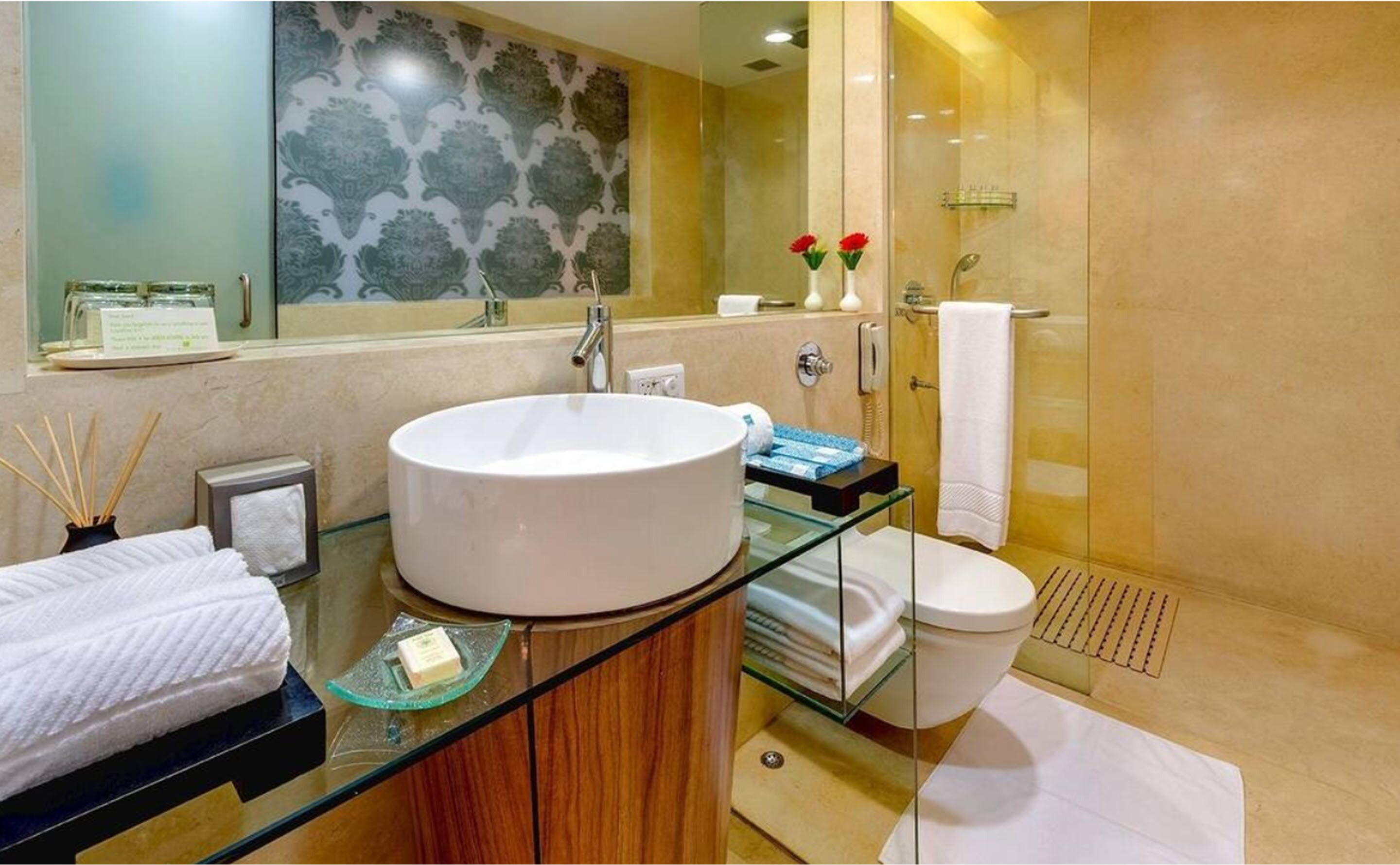 A modern bathroom with a large white sink, glass shower enclosure, and a glass-topped vanity.