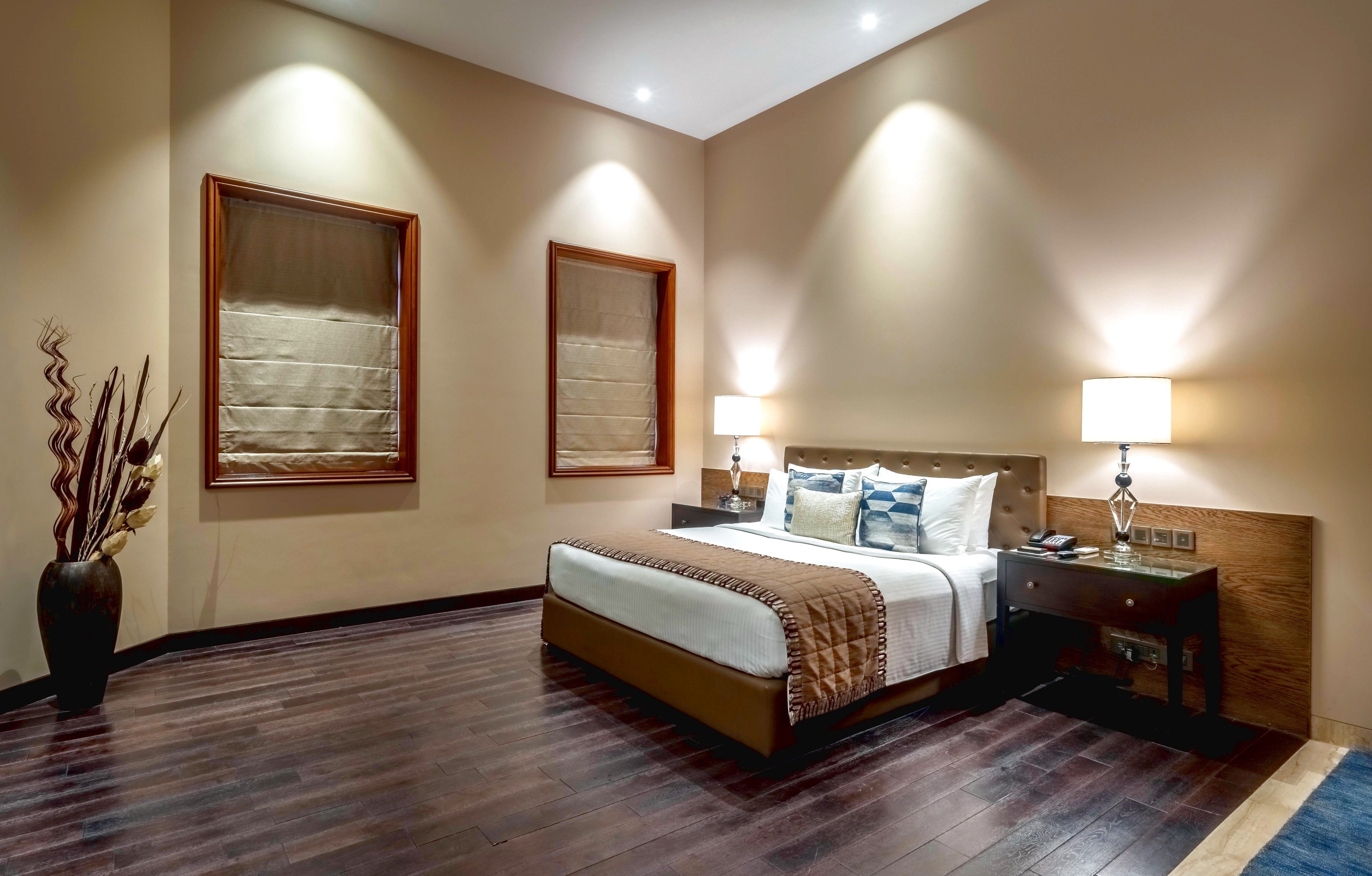 A hotel room with a bed, bedside tables, lamps, and a vase with dried plants.