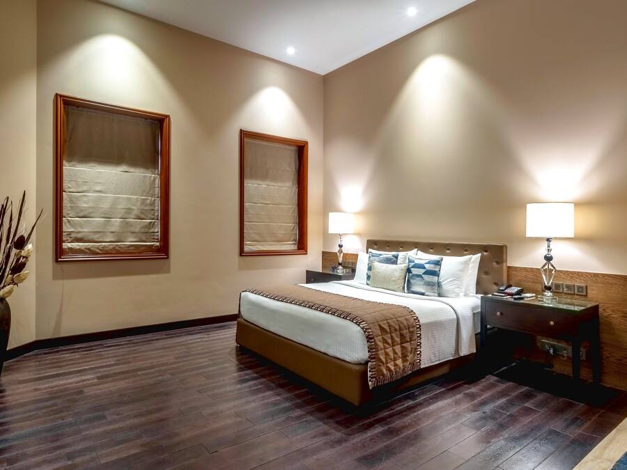 Una habitación de hotel con cama, mesitas de noche, lámparas y un jarrón con plantas secas.