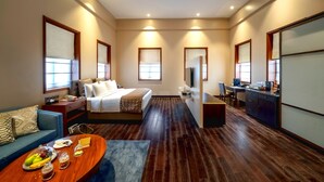 Habitación de hotel con cama, escritorio, sofá y mesa de comedor con frutas y vasos.