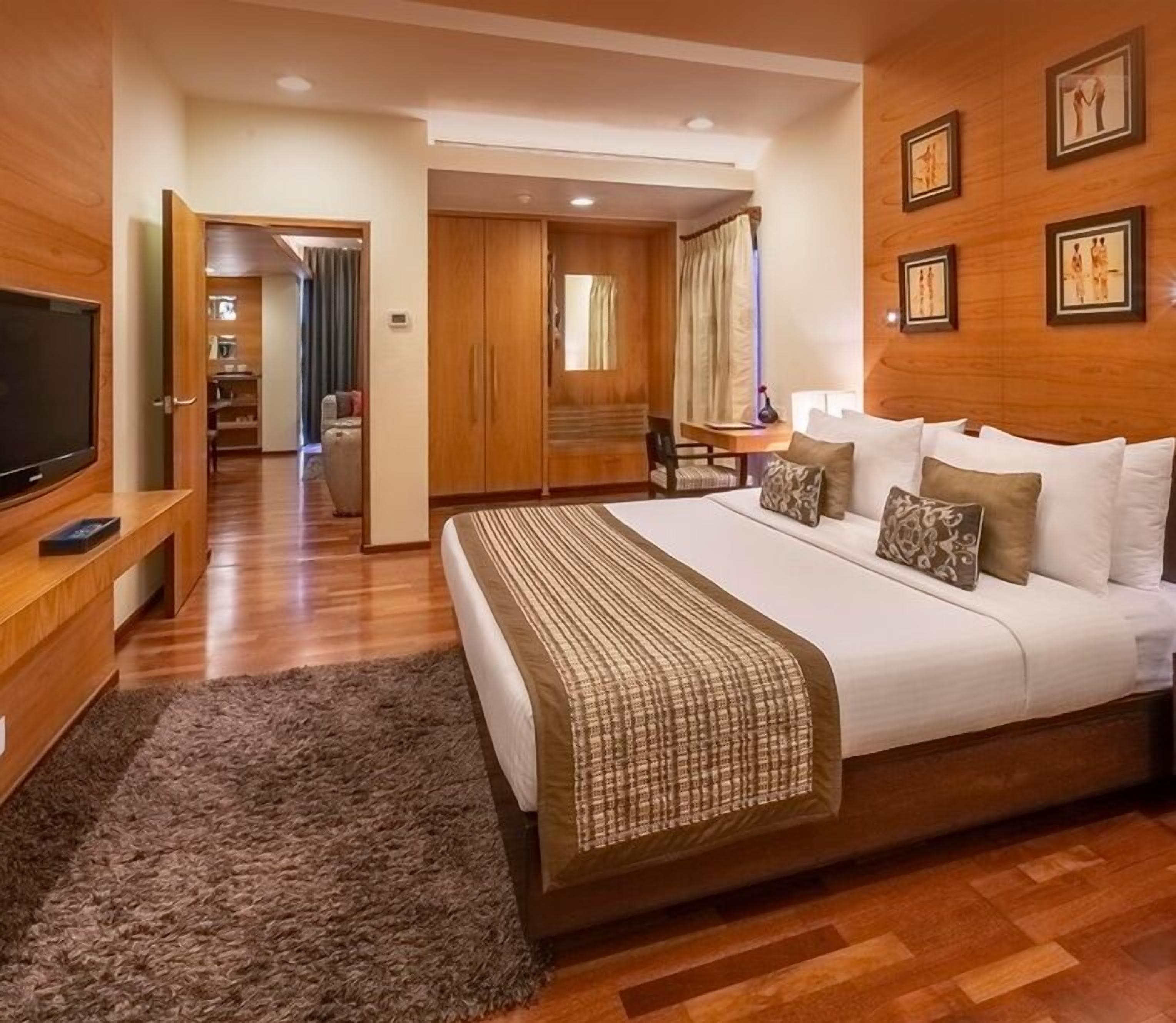 A hotel room with a large bed, a TV on a wooden stand, a desk with a chair, and a wardrobe.