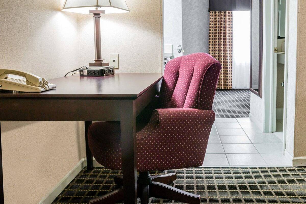 A hotel room with a desk, a telephone, a lamp, and a chair.