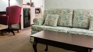 A living room with a floral sofa, a wooden coffee table, and a red armchair. There is a kitchen area in the background with a refrigerator and a microwave. - Econo Lodge & Suites Grand Rapids Airport (Grand Rapids)