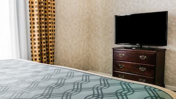 Una habitación de hotel con una cama, un televisor sobre un aparador de madera y una cortina estampada.