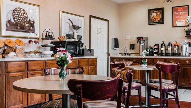 A hotel dining area with a round table, striped chairs, a coffee station, and a kitchen in the background. - Econo Lodge & Suites Grand Rapids Airport (Grand Rapids)