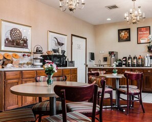 Un comedor de hotel con una mesa redonda, sillas a rayas, una estación de café y una cocina al fondo.