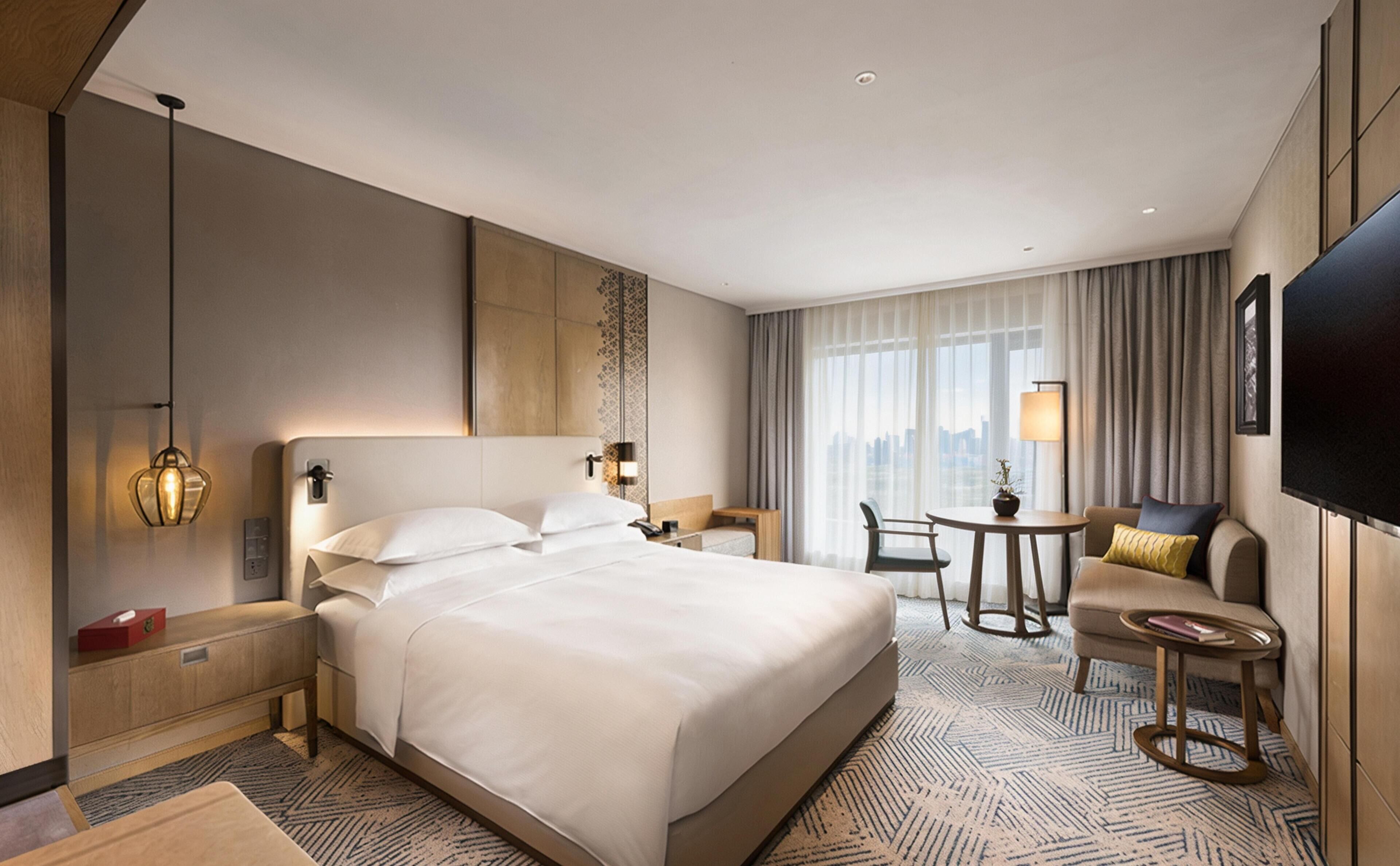 Habitación de hotel con una cama grande, mesitas de noche, escritorio, silla, televisor y vista a la ciudad.