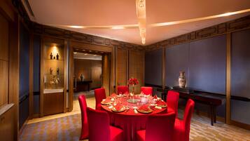 Un comedor con una mesa redonda dispuesta para seis personas, rodeada de sillas rojas. Hay un jarrón con flores sobre la mesa, y la habitación tiene paneles de madera y una alfombra estampada.