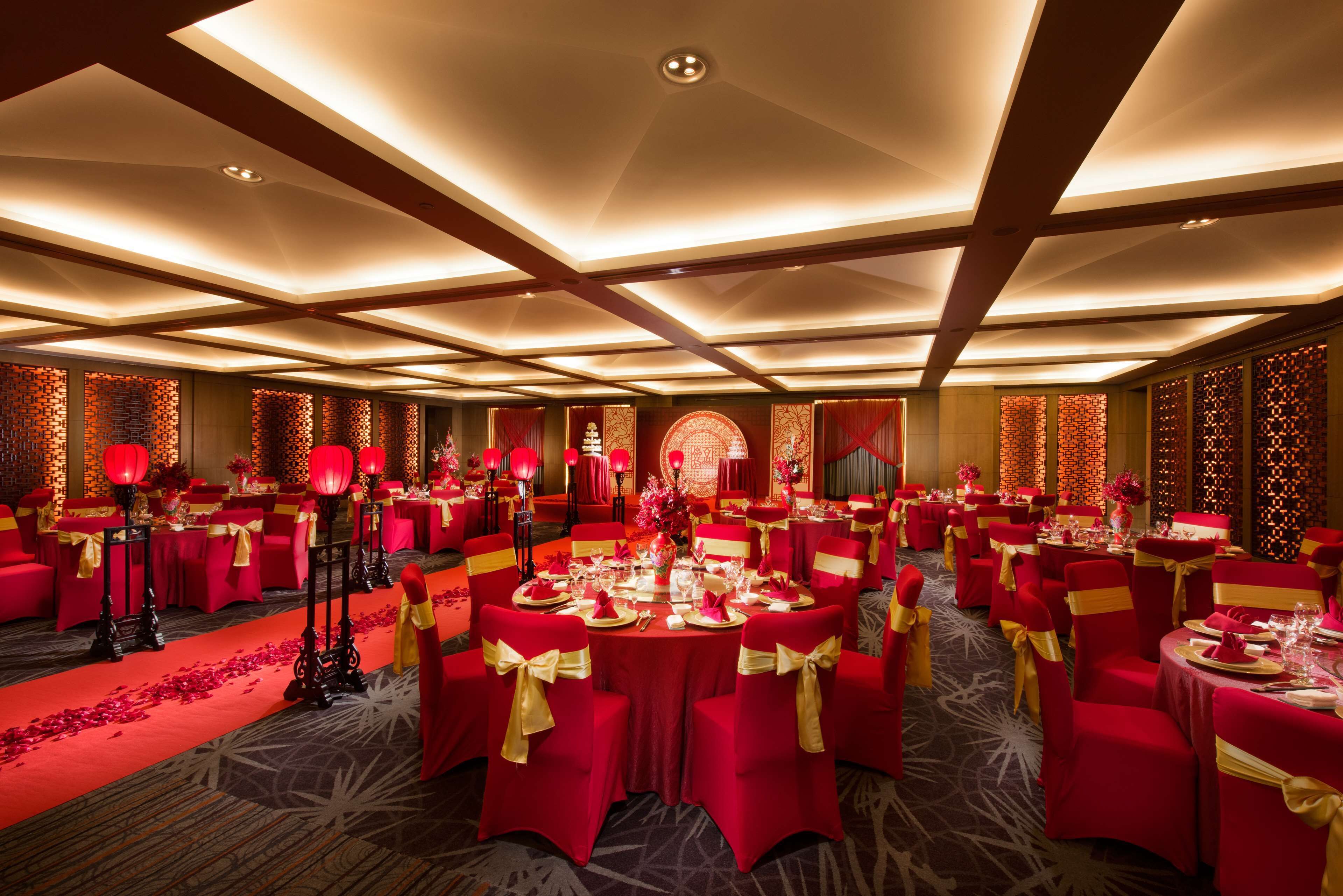A banquet hall with round tables, red chairs, and a carpeted floor.